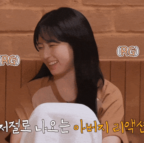 a woman is smiling and holding a towel in front of a brick wall with foreign writing on it