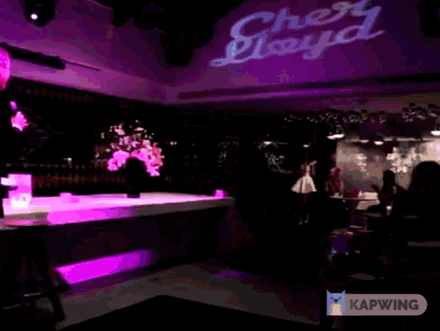 a woman singing into a microphone next to a man on a stage with kapwing written on the bottom