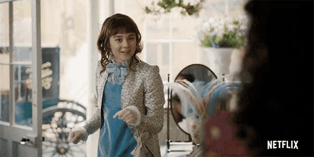 a girl in a blue dress is standing in a room with a netflix logo in the corner