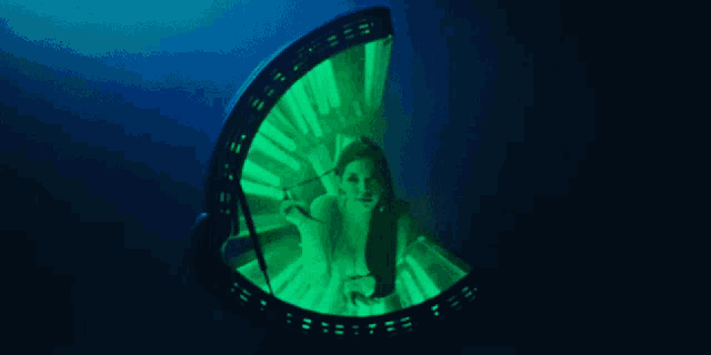 a woman is sitting in a tanning booth with green lights behind her
