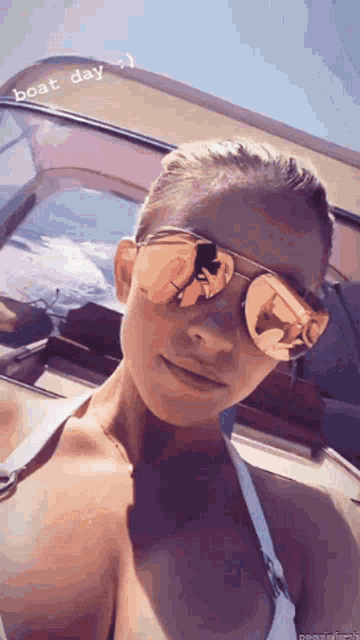 a woman wearing sunglasses and a bikini is taking a selfie on a boat .