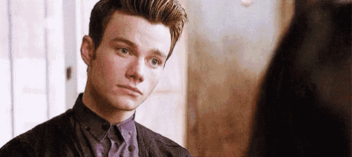 a young man in a sweater and tie is looking at another man .