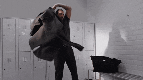a man in a suit is standing in a locker room with a bag on a bench