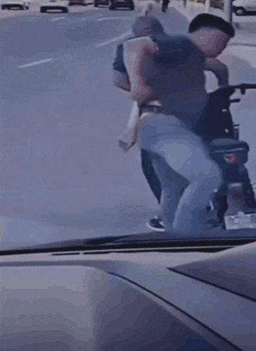 a man in a grey shirt is walking down a street with a motorcycle in the background