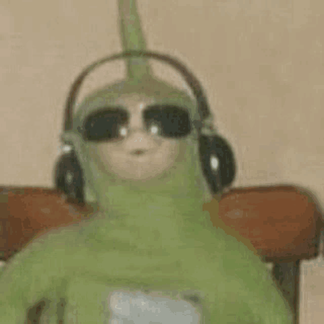 a green doll wearing headphones and sunglasses is sitting on a chair .