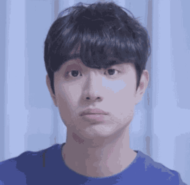 a close up of a young man making a funny face while wearing a blue shirt .