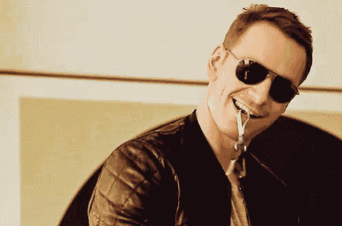 a man wearing sunglasses and a leather jacket holds a key in his mouth
