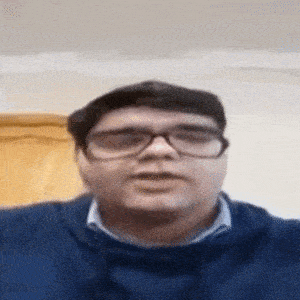 a man wearing glasses and a blue sweater is talking .