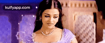 a woman in a purple dress and a necklace is standing in front of a window .