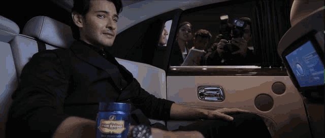 a man sits in the back seat of a car holding a can of san marino