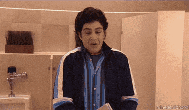 a man in a blue and white striped shirt is standing in a public restroom ..