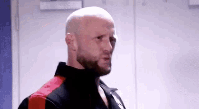 a bald man with a beard is standing in a locker room looking at the camera .