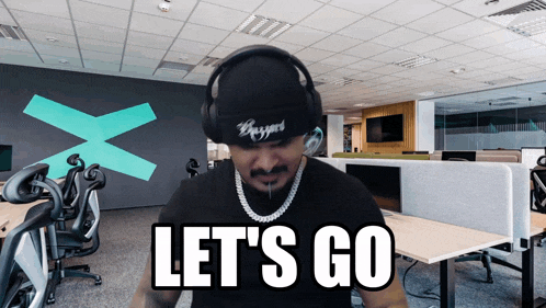 a man wearing headphones and a beanie says let 's go in an office