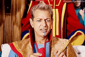 a man in a colorful costume is sitting on a couch and making a funny face .