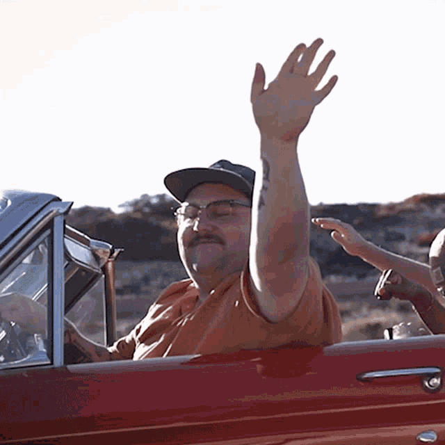 a man with a tattoo on his arm is waving from the window of a red car