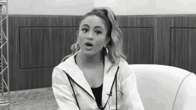 a black and white photo of a woman sitting in a chair talking .