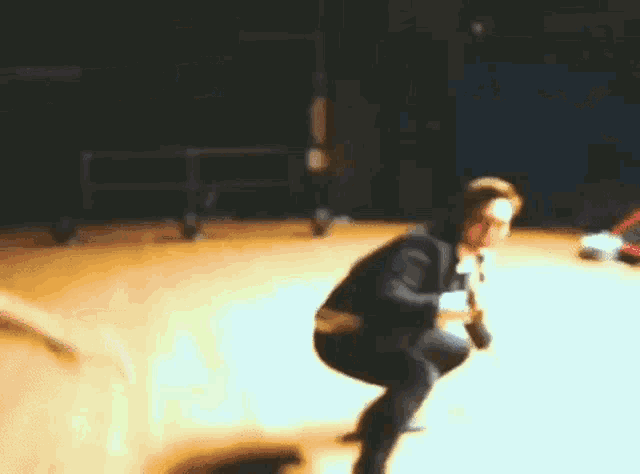 a man in a suit is squatting down on a stage with a microphone in his hand