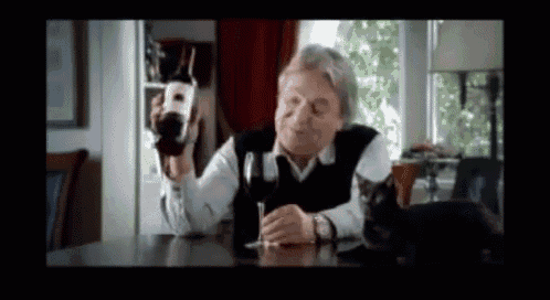 a man is sitting at a table holding a bottle and a glass of wine