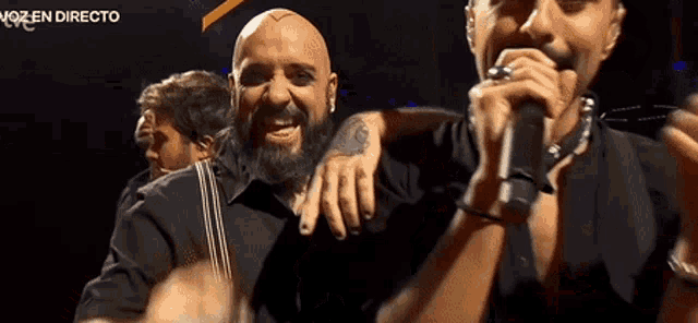 a man with a tattoo on his arm is singing into a microphone in front of a sign that says " voz en directo "