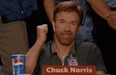 a man is sitting at a table with a sign that says chuck norris .