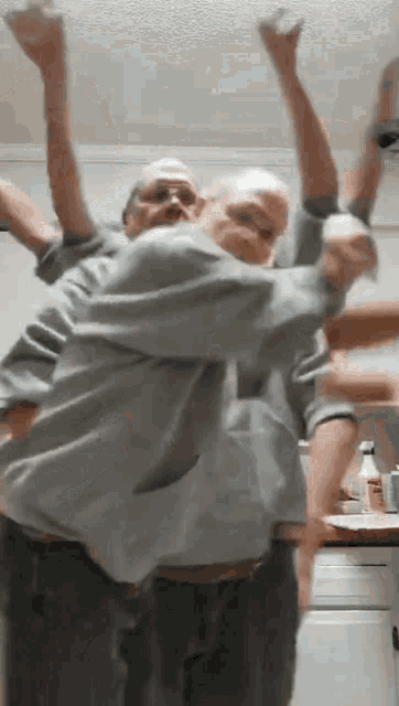 two men are dancing in a kitchen with their hands in the air .