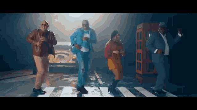 a group of men and women are dancing on a crosswalk in front of a telephone booth .