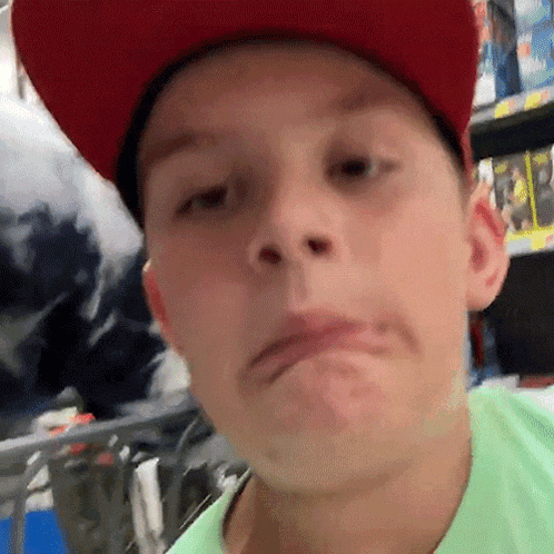 a young boy wearing a red hat and a green shirt is making a funny face