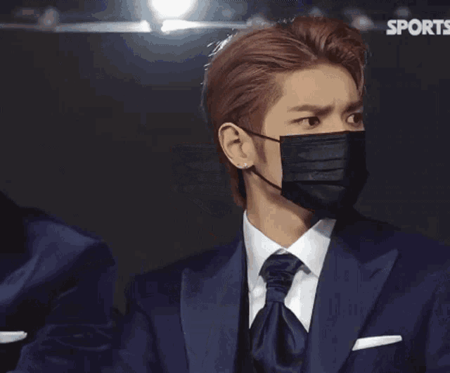 a man in a suit and tie wearing a black mask with the name taeyong on the bottom right