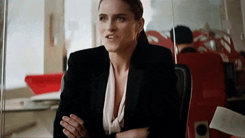 a woman in a black suit is sitting in a chair