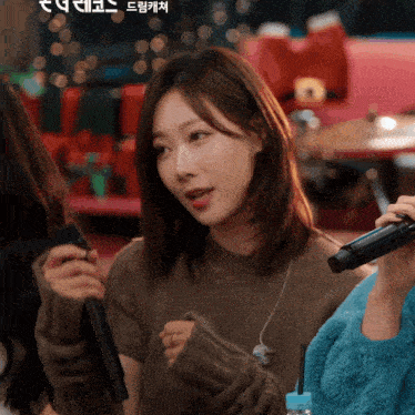 a woman in a brown sweater holds a microphone in her hand