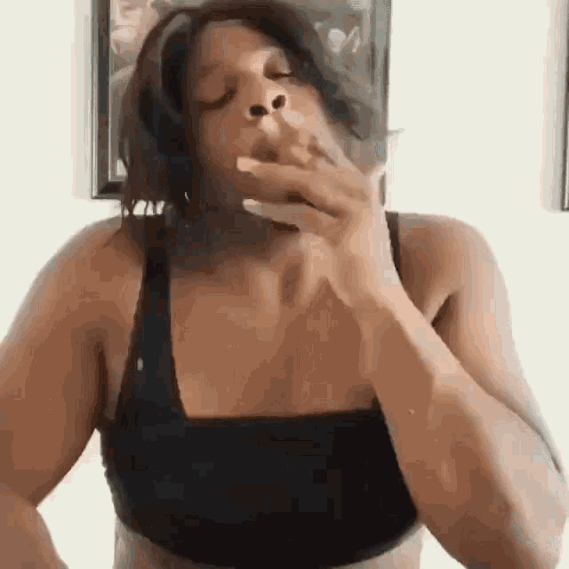 a woman in a black bra is smoking a cigarette in front of a picture .