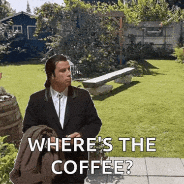 a man in a suit is standing in a garden and asking where 's the coffee .