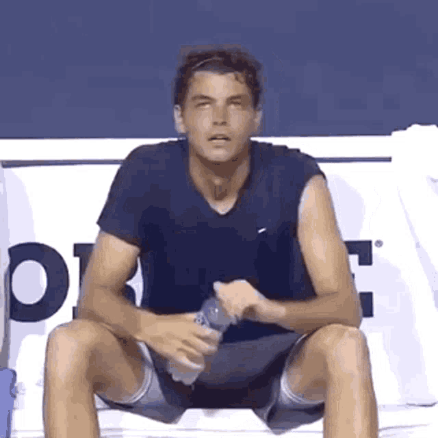 a tennis player is sitting on a bench holding a bottle of water .