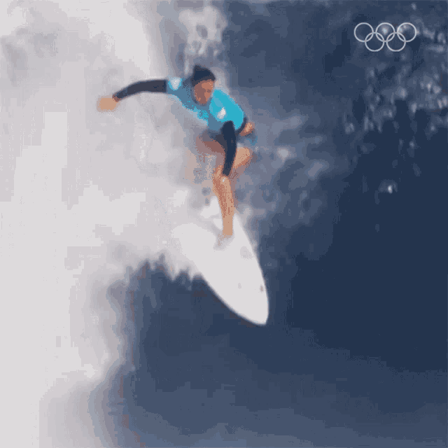 a woman is riding a wave on a surfboard with the olympics logo in the background