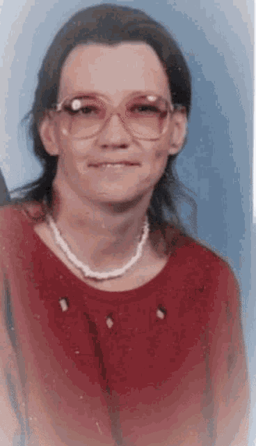 a woman wearing glasses and a pearl necklace is smiling