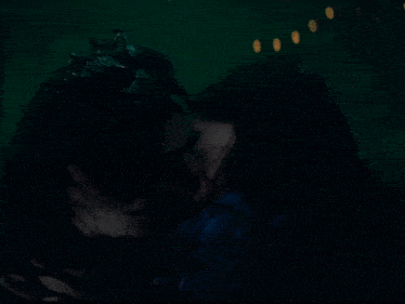 a woman with a crown kisses another woman in a dark room