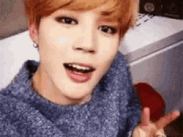 a young man in a blue sweater is making a peace sign with his hand .