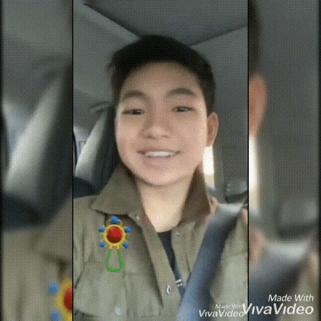a young boy is smiling while sitting in a car with a sun sticker on his jacket .