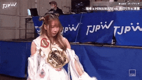 a woman in a white dress is standing in front of a blue wall with tjpw written on it .
