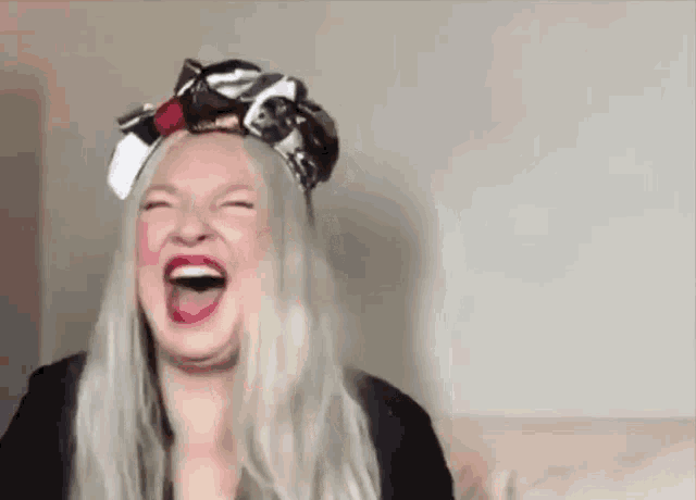 a woman wearing a head scarf is laughing with her mouth open and her eyes closed .