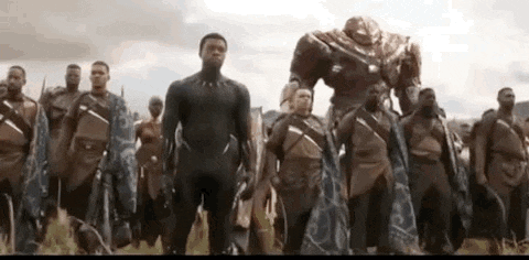 a group of men are standing next to each other in a field . one of the men is a black panther .