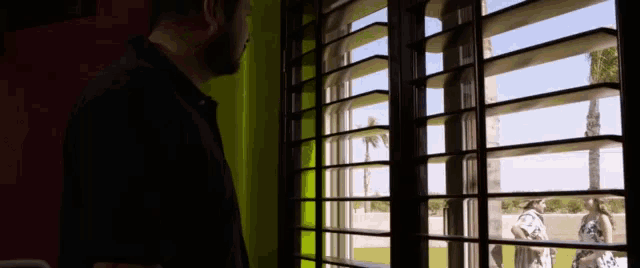 a man looking out a window with shutters open