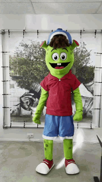a green mascot wearing a red shirt and shorts