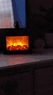a fire burning in a dark room with a blue sky behind it