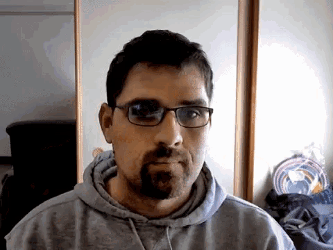 a man with glasses and a beard is wearing a grey sweatshirt