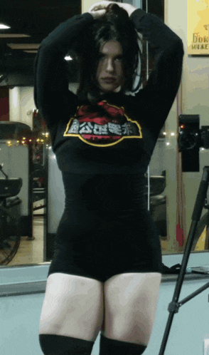 a woman in a black shirt with chinese writing on it stands in front of a tripod