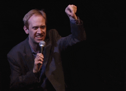 a man in a suit holds a microphone in front of a black background that says yes