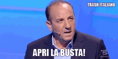 a man in a suit and tie is talking into a microphone and says apri la busta !