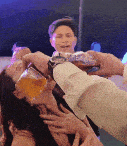 a man is holding a glass of beer over another man 's face