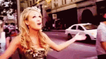 a woman is standing on a street with her arms outstretched and a white car in the background